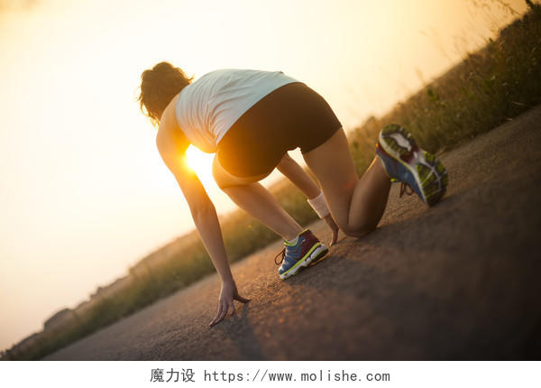 夕阳下年轻女人正在准备起跑励志运动健身户外跑步